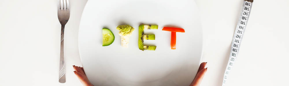 White plate with the word "diet" spelt out in vegetables, with a measuring tape wrapped around the plate and a fork beside it White plate with the word "diet" spelt out in vegetables, with a measuring tape wrapped around the plate and a fork beside it